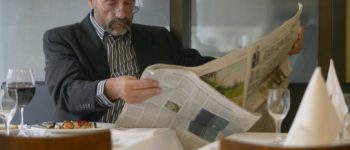 homme lisant son journal avec un verre de vin